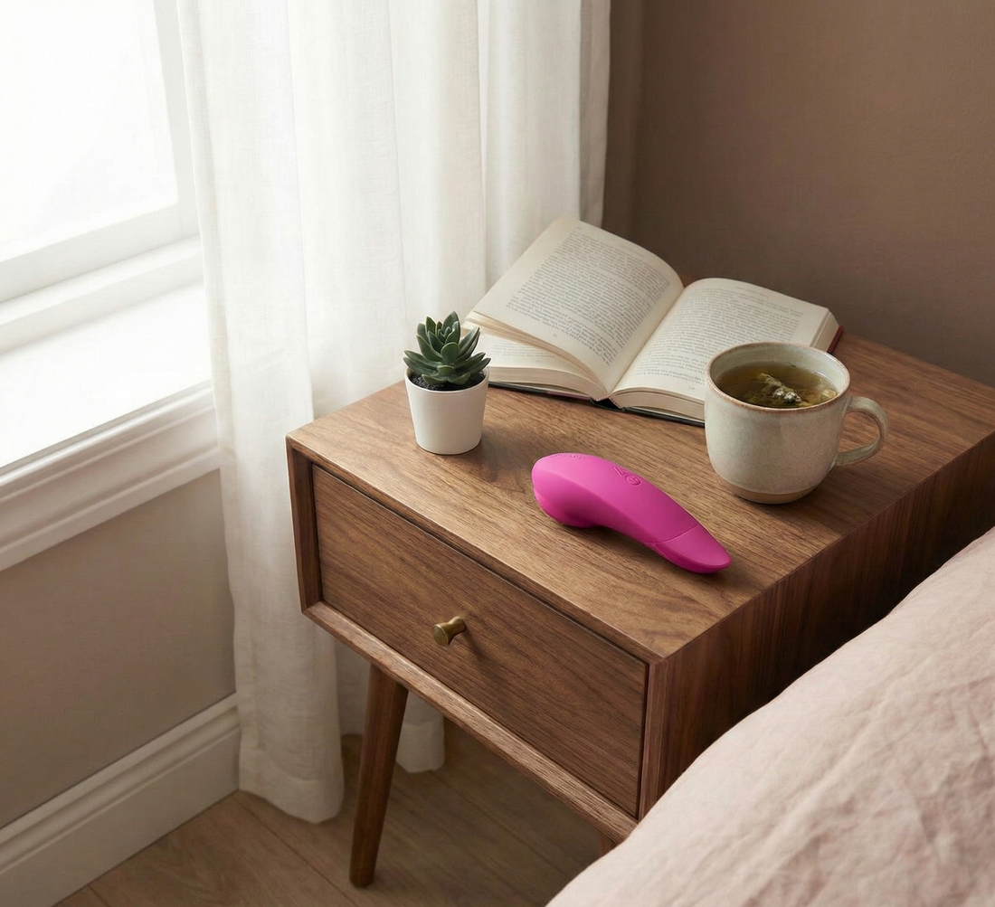 Womanizer Liberty 2 rose posé sur une table de nuit en bois avec un livre et une tasse de thé, illustrant une routine bien-être et plaisir signée Espace-Love.